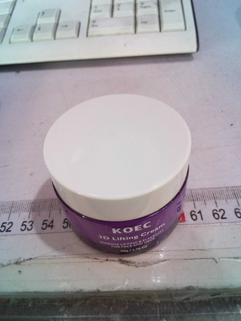 Close-up of the KOEC 3D Lifting Cream jar with purple body and white lid, placed on a surface with a measuring tape nearby